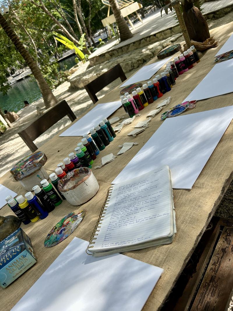 The table set and waiting: paints lined up beside an open journal, the lagoon beyond.