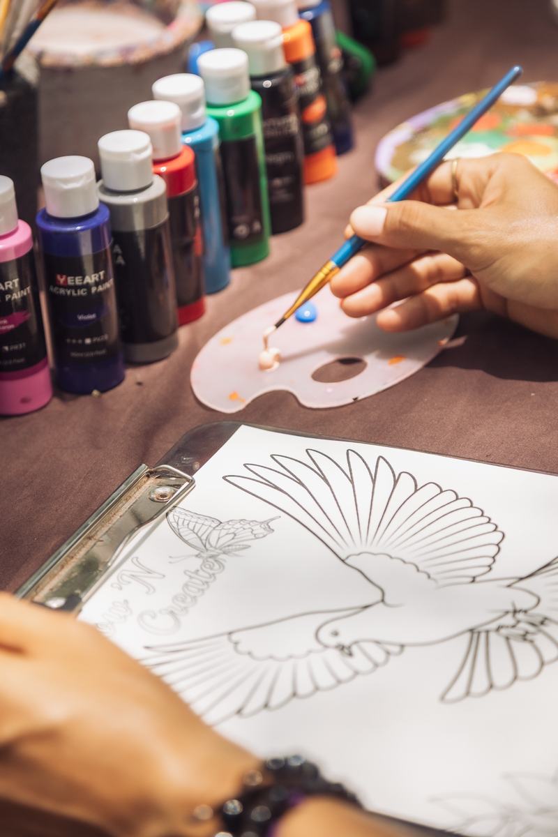 A hand mixing paint on a palette beside a SoulFlow ’N Create drawing of a bird.