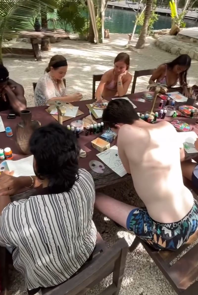 People settling in to paint around the table, water shining behind them.