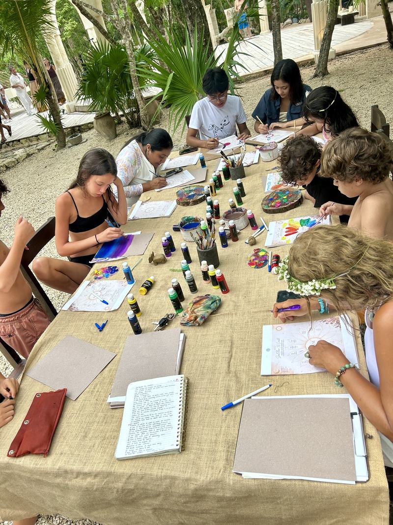 People gathered closely around a painting table, absorbed in colour and conversation.