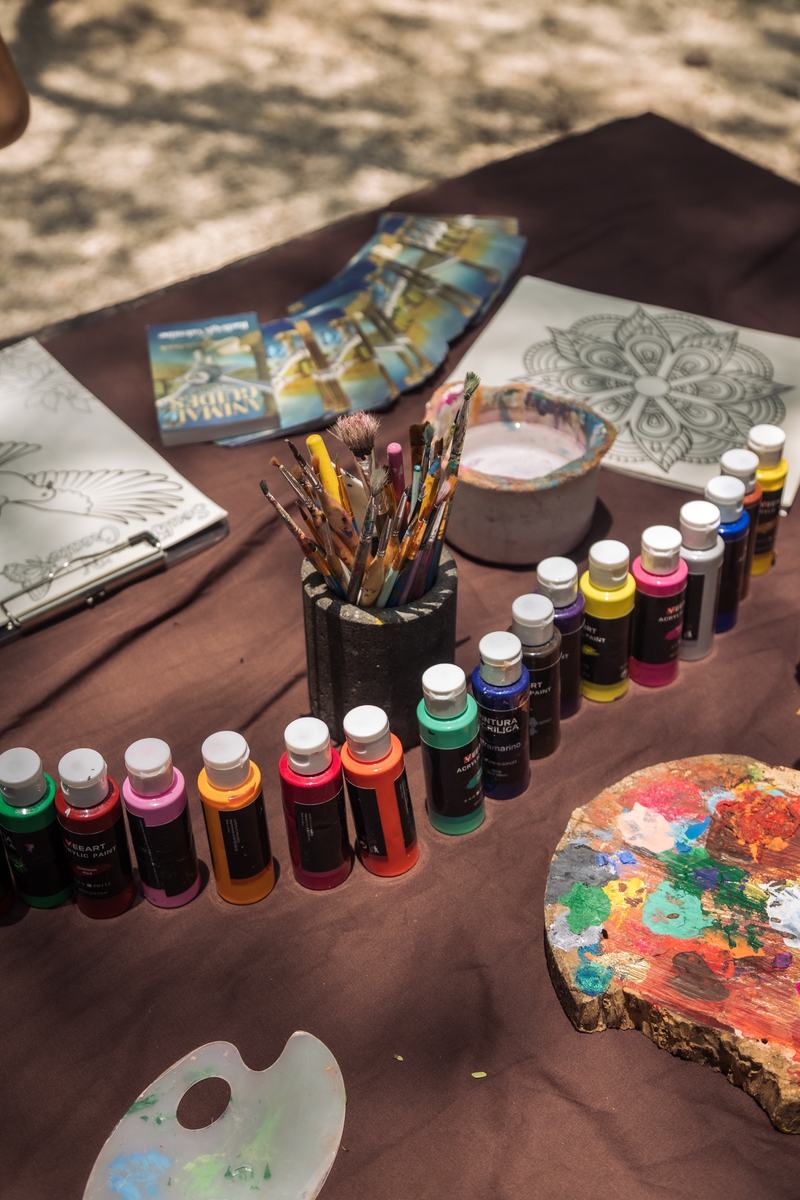 Rows of paint bottles, brushes and a wooden palette laid out on the table.