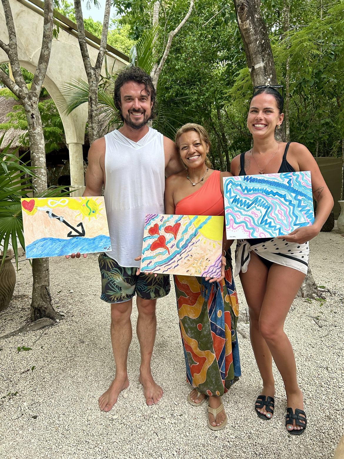 Three people standing together, each holding up the painting they made.