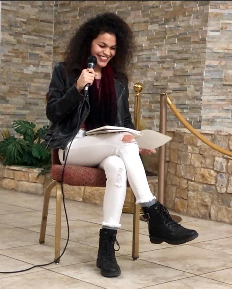 Cyndiii Deusa glancing down at her poetry, smiling.